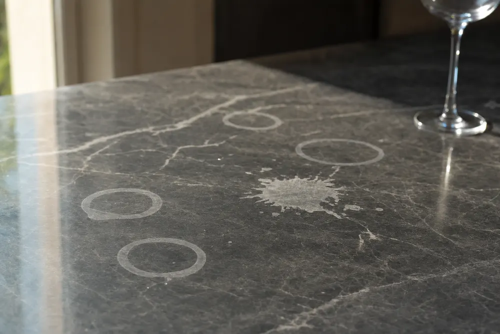 Dull etch rings and a splash-shaped etch mark interrupting the polish of a dark marble benchtop