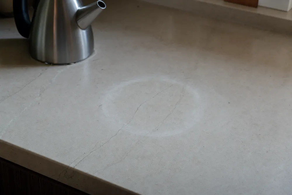 A pale cloudy heat ring in a honed limestone benchtop near a kettle