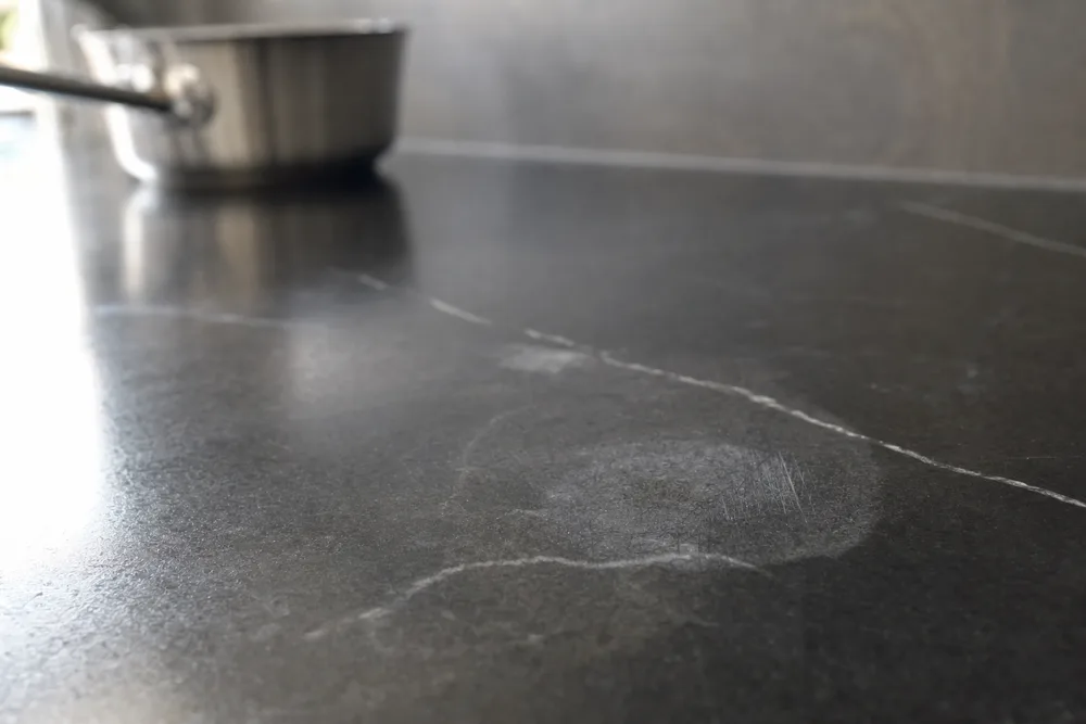 A pale heat mark and fine scratches on a dark stone benchtop